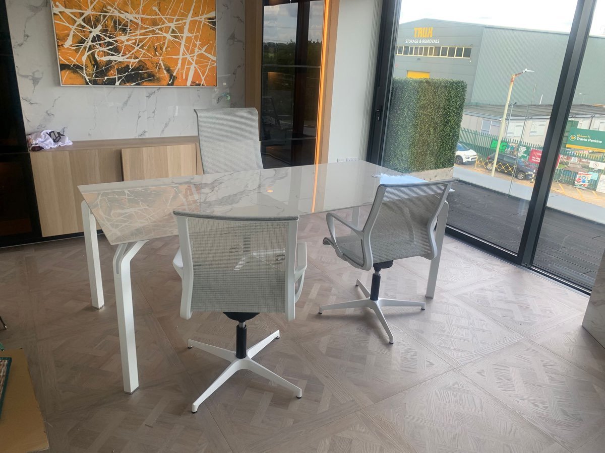 A marble meeting table and mesh chairs assembled in a bright showroom, with artwork mounted on the wall